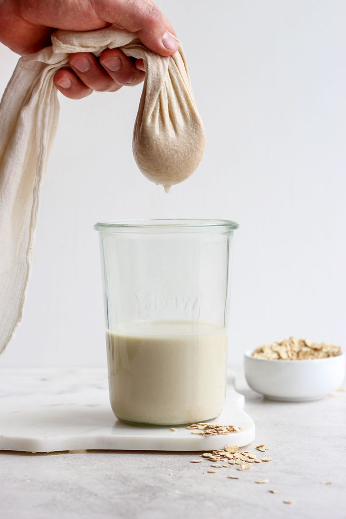 filtering out oat milk in a tea towel