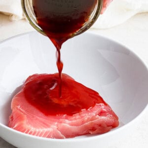 A person is pouring a sauce on an ahi poke bowl.