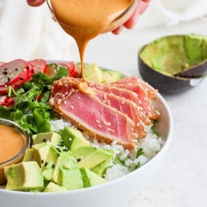 a person drizzling a creamy tahini sauce on a nutritious ahi poke bowl.