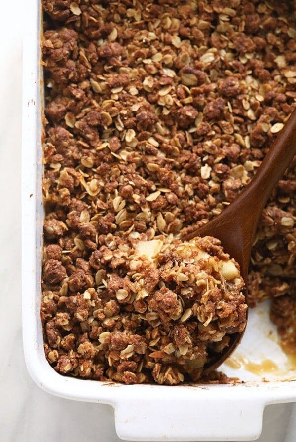 A white baking dish with a spoonful of granola in an apple crisp recipe.