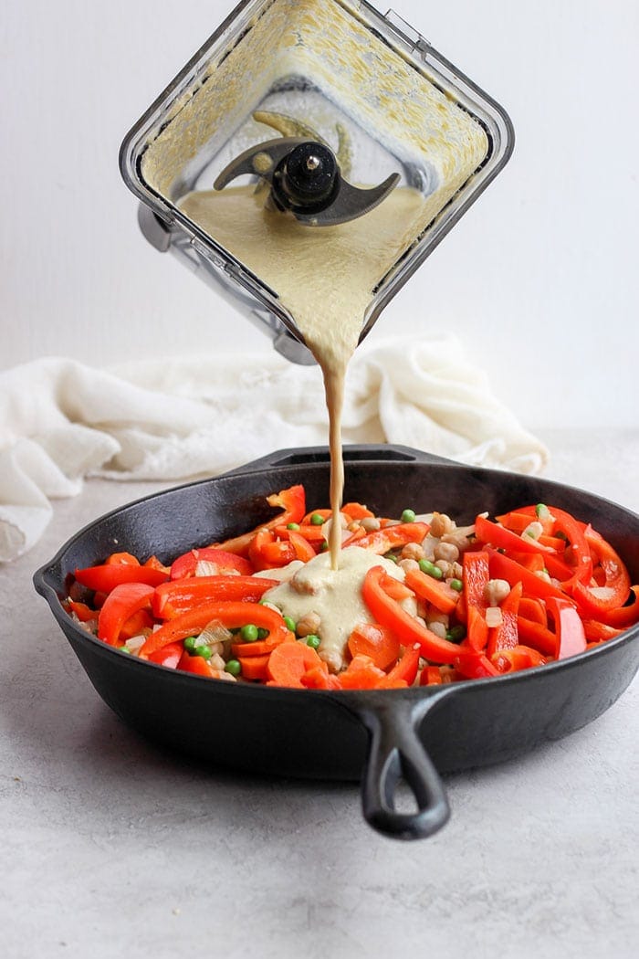 creamy cashew curry sauce being poured over sautéed veggies