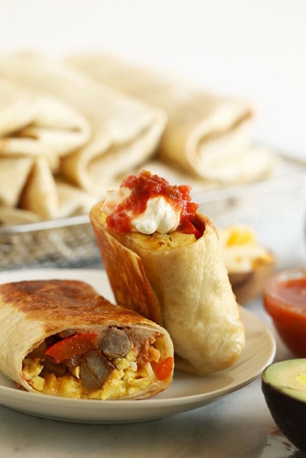 Fajita breakfast burritos with avocado and salsa on a plate.