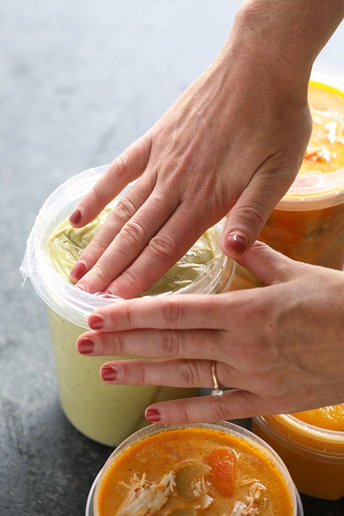 Placing plastic wrap on top of soup container to prevent freezer burn