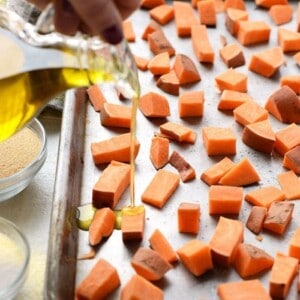 Drizzling olive oil onto sweet potato cubes on a baking sheet.