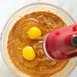 two eggs in a bowl of pumpkin cheesecake bars.