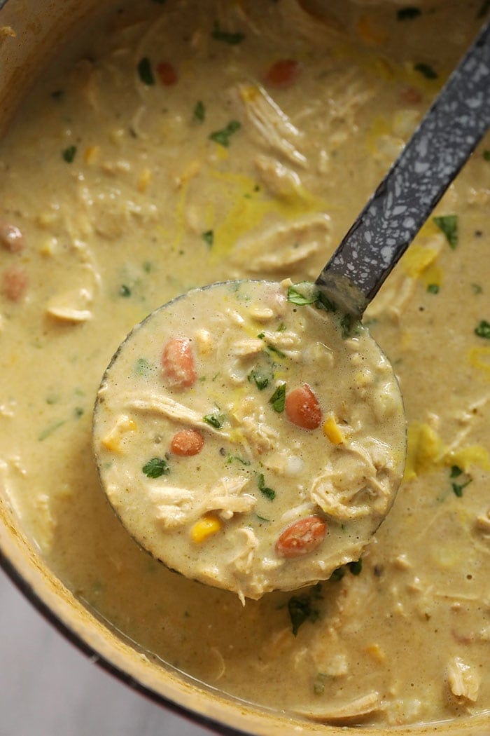 white bean chicken chili on a ladle in a dutch oven.