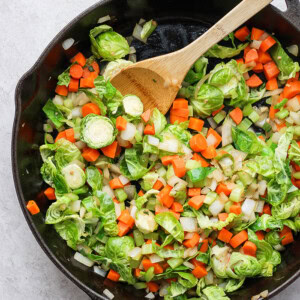 Brussels sprouts sautéed in a skillet with a wooden spoon.