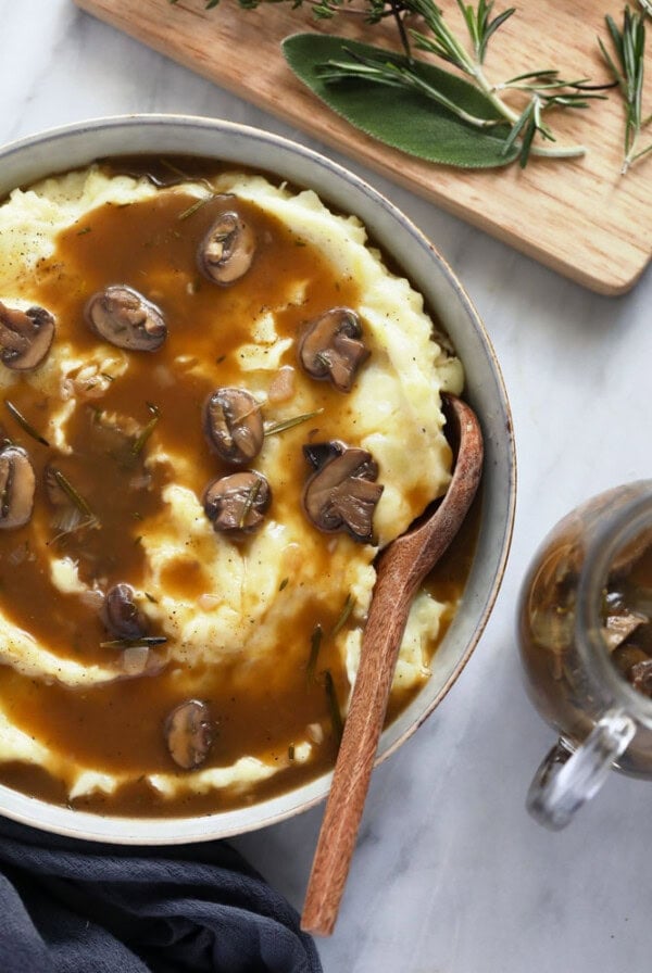 a bowl of vegan mashed potatoes topped with mushroom gravy and sprigs of rosemary.