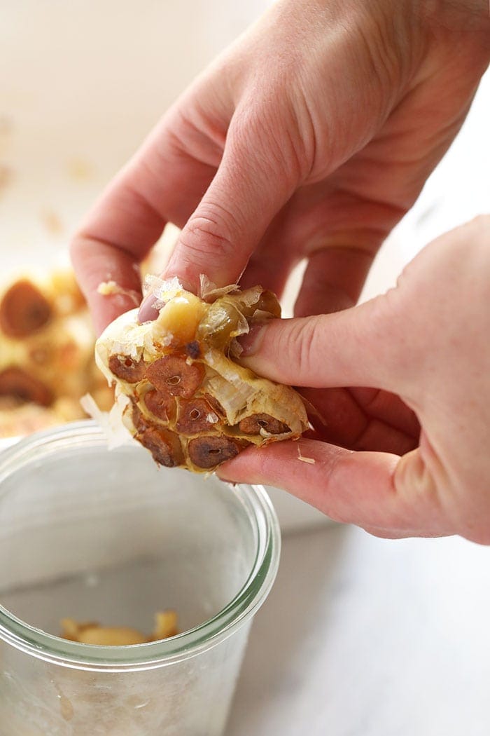 pushing garlic cloves out of the bulb after roasting