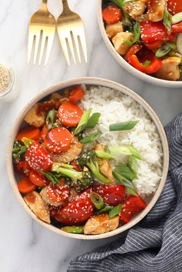 Two bowls of teriyaki chicken stir fry on a marble table.