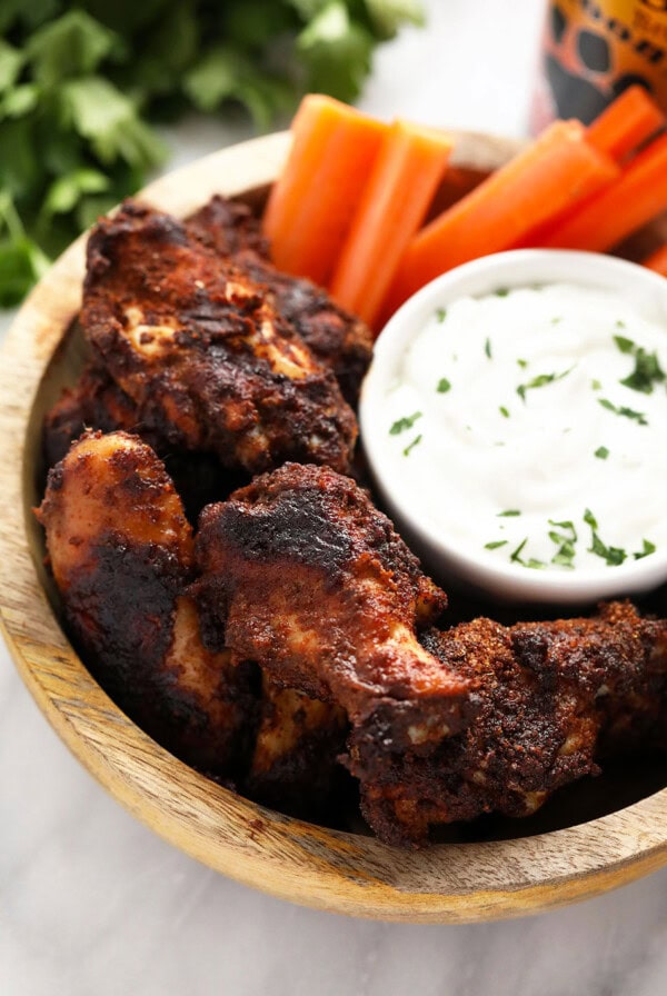 Dry rub chicken wings served in a wooden bowl with dipping sauce.