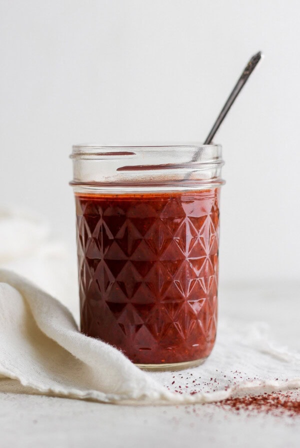 A jar of homemade enchilada sauce with a spoon on a white cloth.