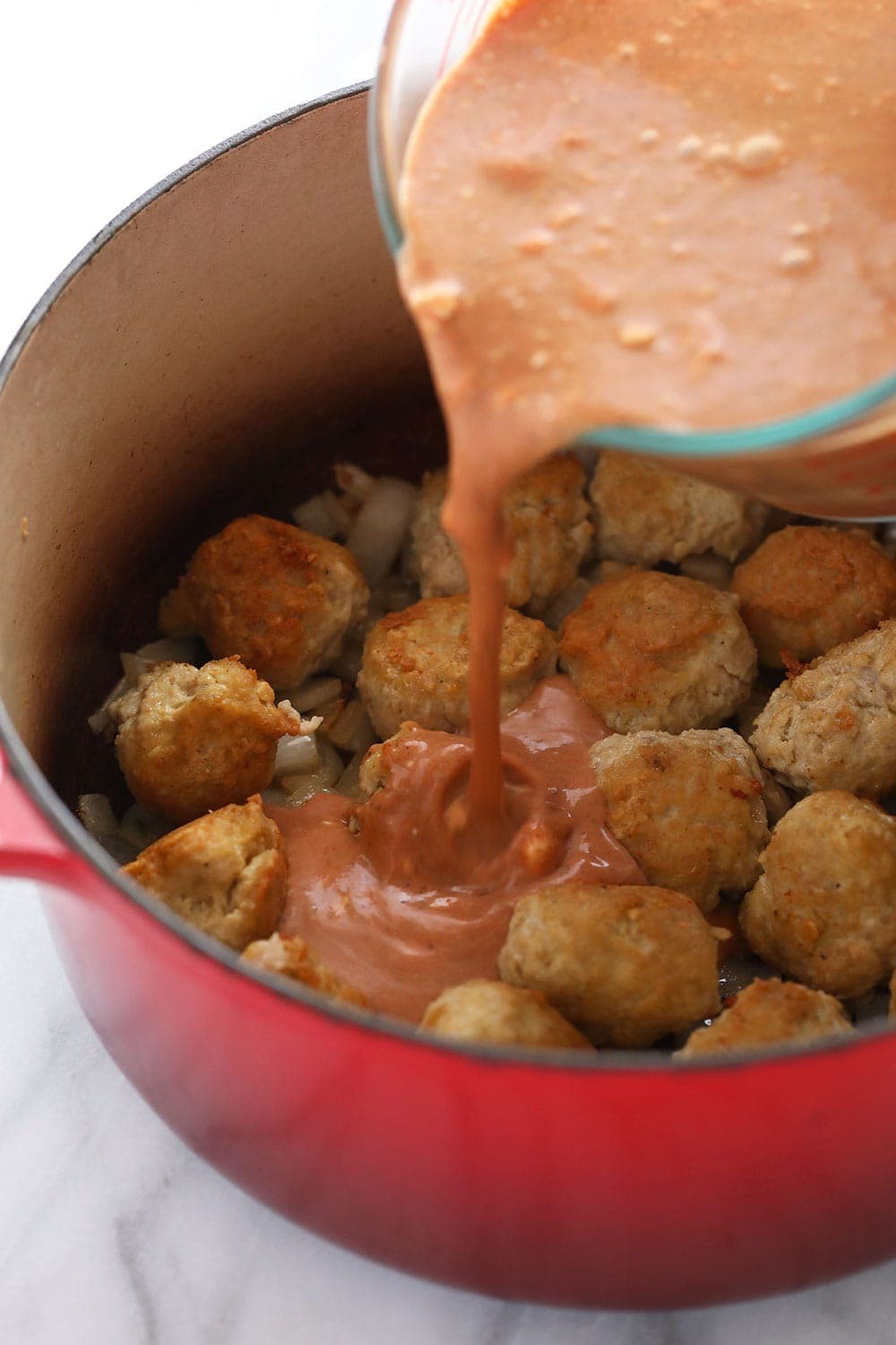 Pouring tikka masala sauce over the meatballs