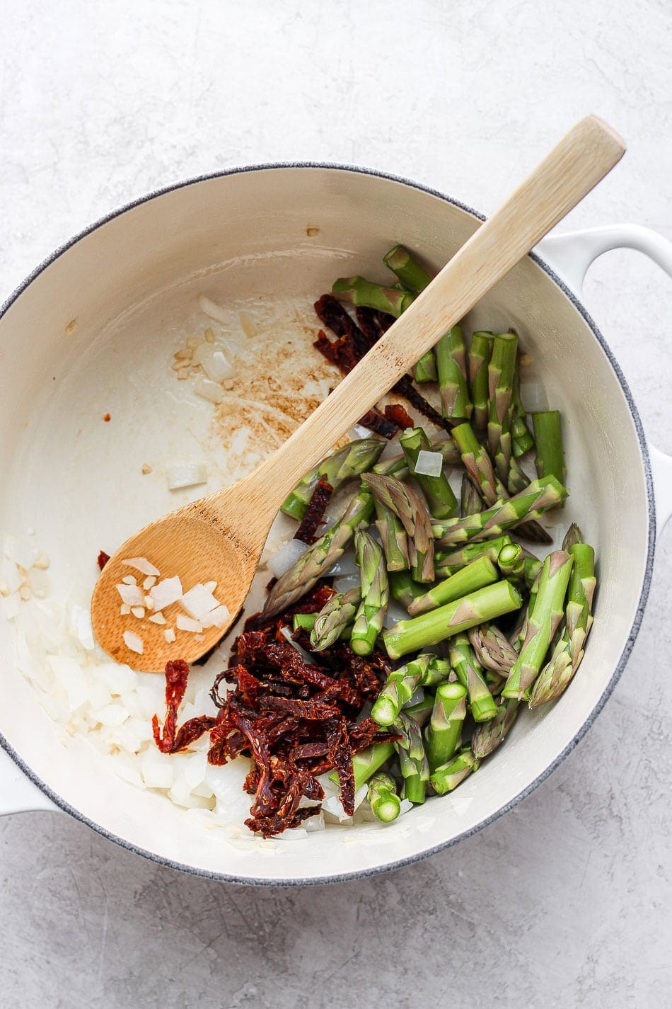 asparagus, sun-dried tomatoes and onions in a dutch oven ready to be sauteed