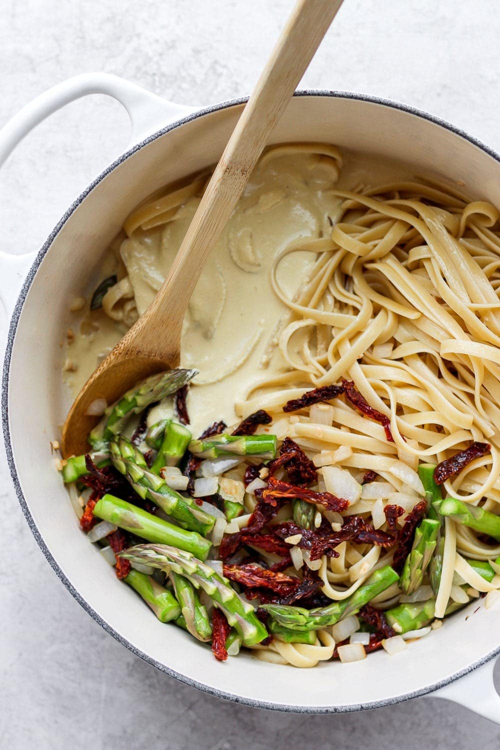 creamy vegan asparagus pasta in a dutch oven ready to be tossed together with veggies and creamy sauce