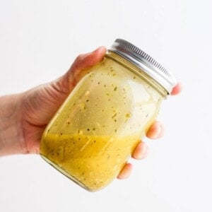 a hand holding a jar of Greek salad dressing.