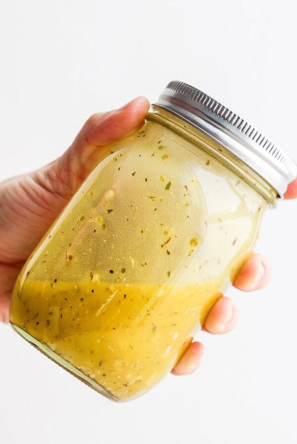 a hand holding a jar of Greek salad dressing.