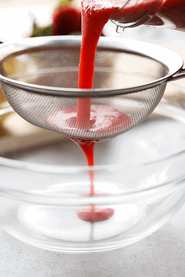 fresh strawberry puree being strained through a sieve