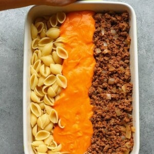 A person holding a hamburger casserole dish with the ingredients before they're mixed together.