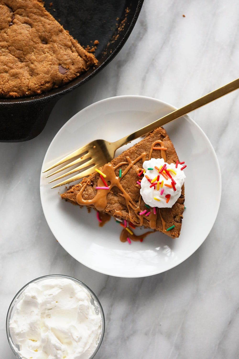 slice of cookie cake on plate with whipped cream and sprinkles