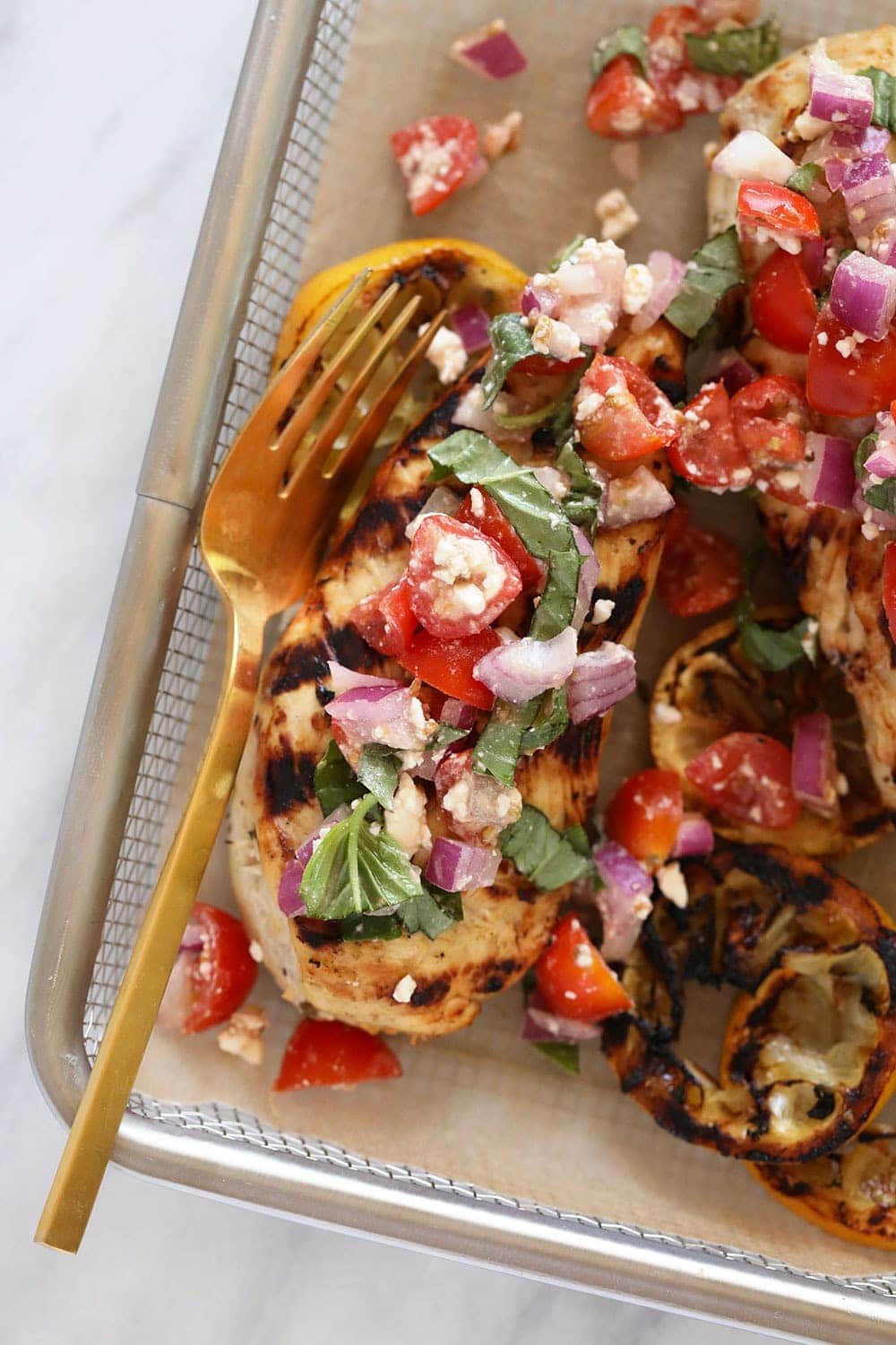 Grilled Greek lemon chicken with greek salad on top of the chicken breast. 