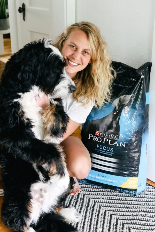 a woman posing with her dog next to a bag of dog food.