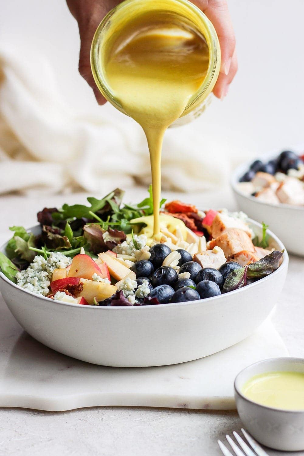 pouring honey mustard dressing onto chicken salad in bowl.