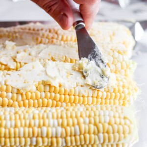 a person slicing grilled corn on the cob with a knife.