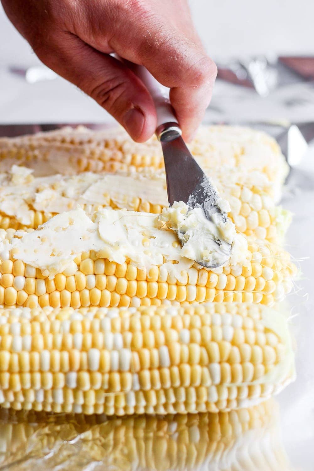 softened butter being spread on ears of corn before it goes on the grill