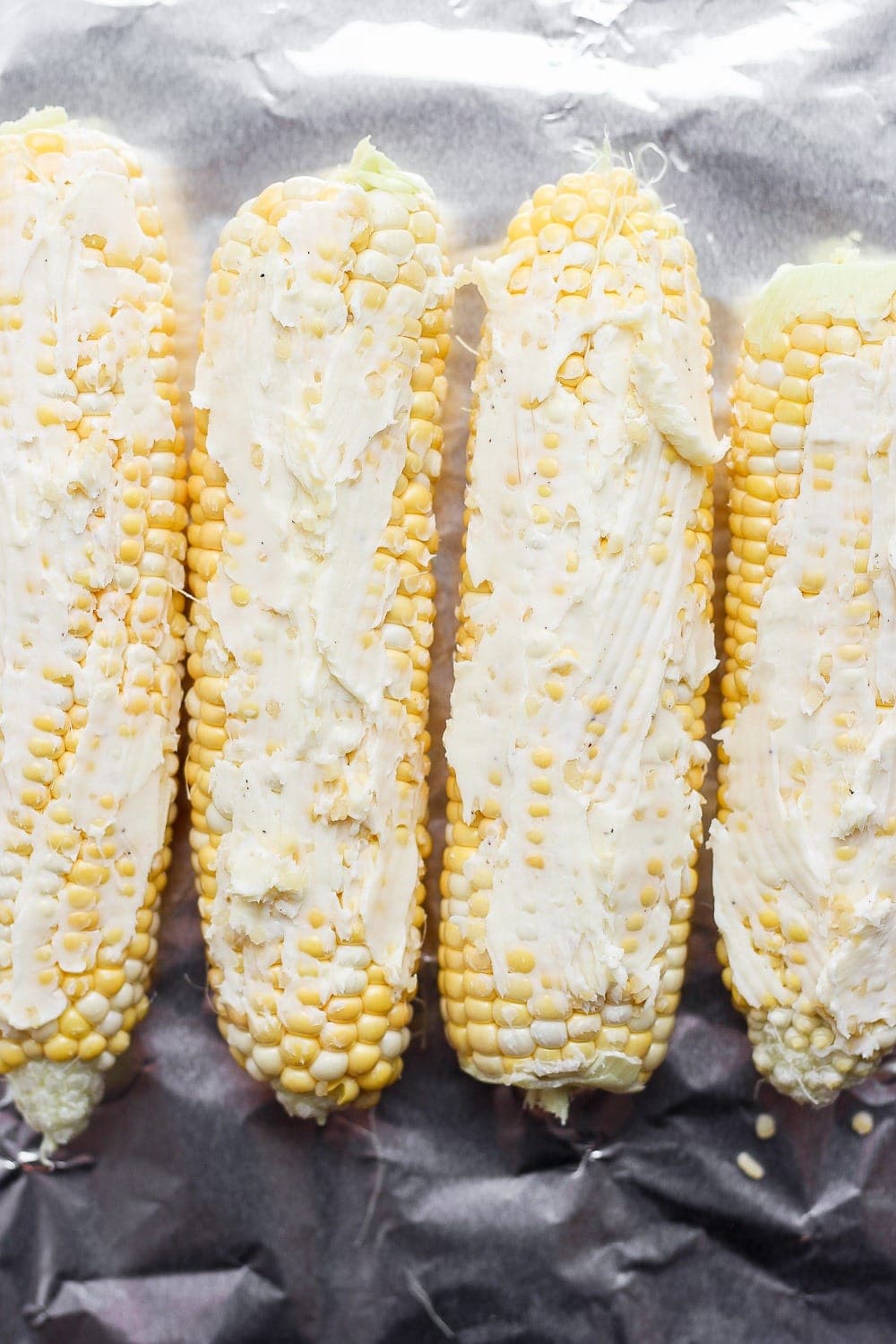 corn on the cob with butter spread on it, laid atop tin foil and ready to be made into a foil pack