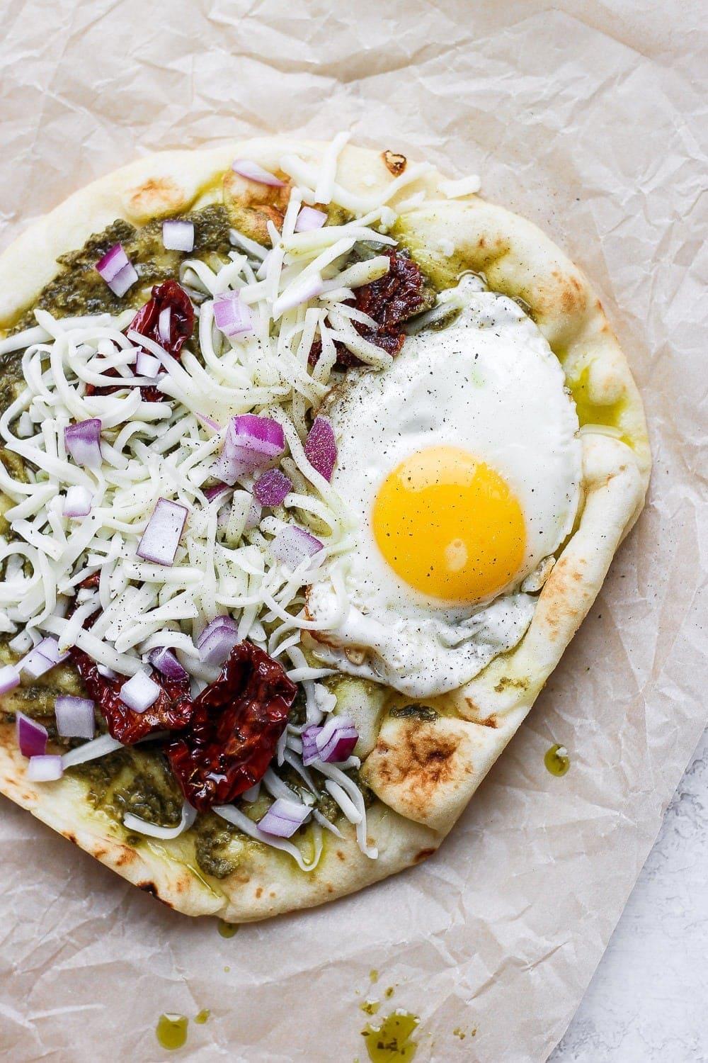 Naan pizza topped with pesto, sun dried tomatoes, cheese, and a fried egg. 