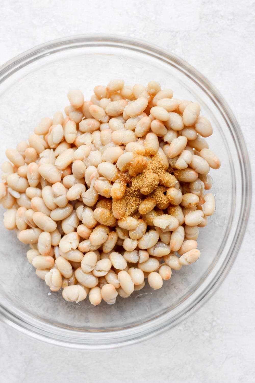 white navy beans and spices in a bowl ready to be mixed into shrimp salad