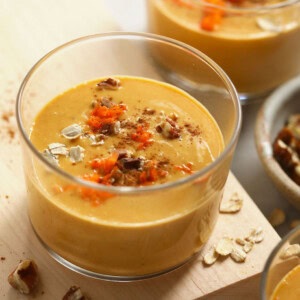 A bowl of carrot cake smoothie with oats on a wooden cutting board.