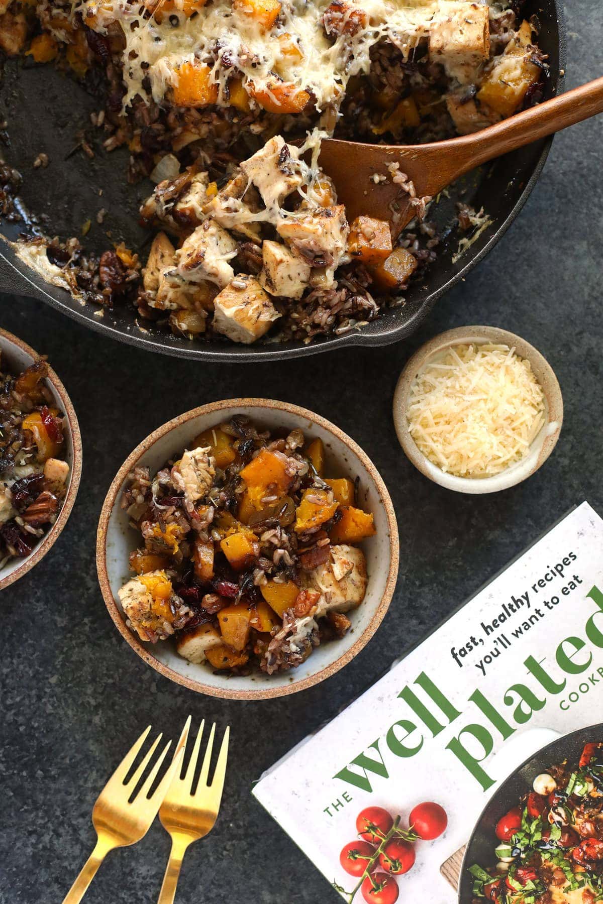 butternut squash wild rice casserole in a cast iron pan being scooped with a wooden spoon