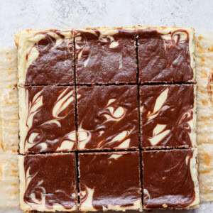 white swirled bars atop a square of chocolate cheesecake on a white surface.