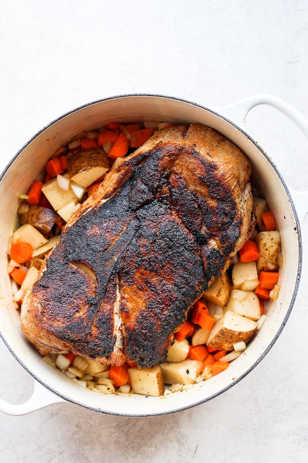 pork shoulder surrounded by veggies and ready to be roasted