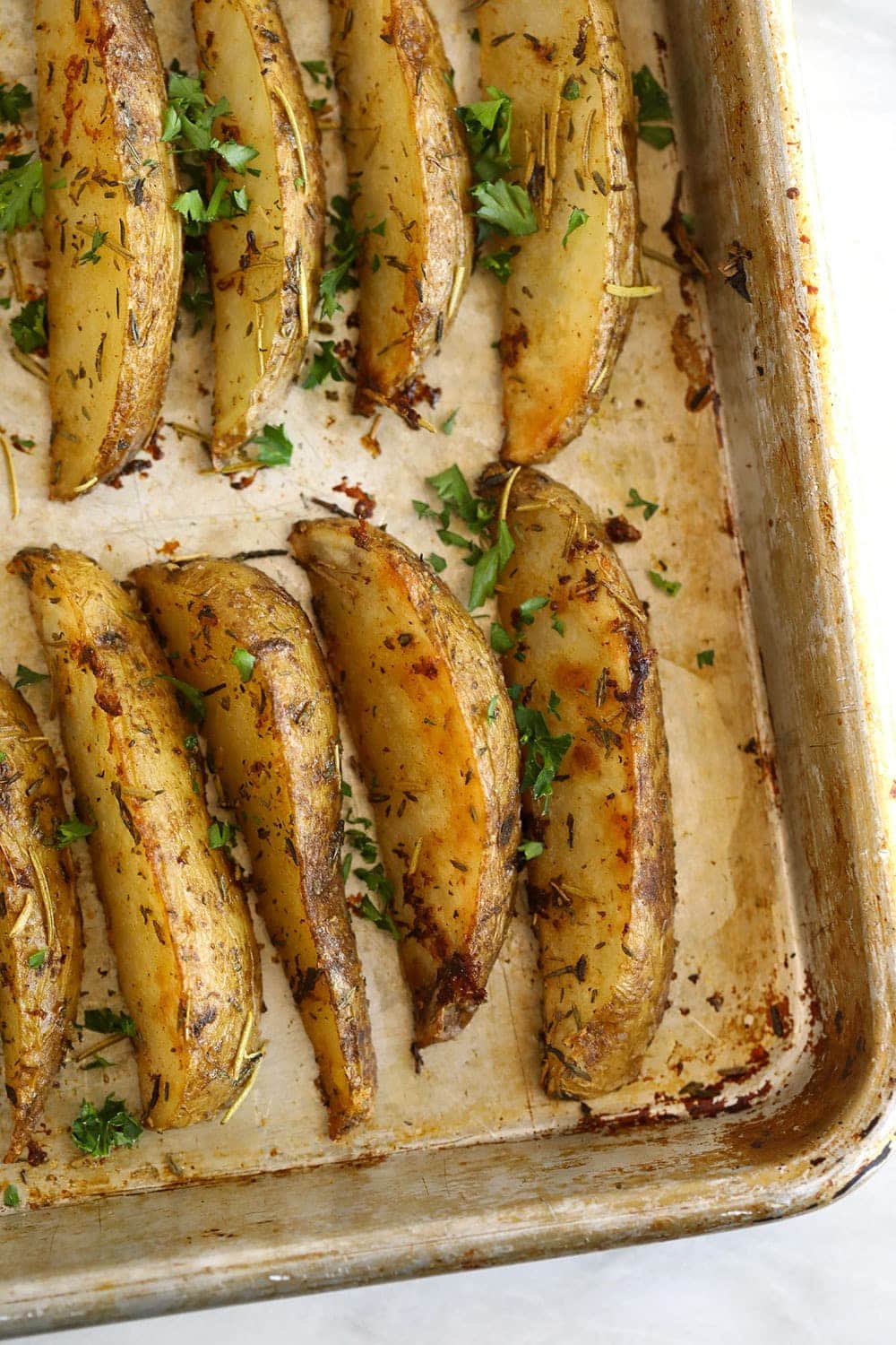 Potato wedges on a baking sheet with fresh parsley sprinkled over the potato wedges. 