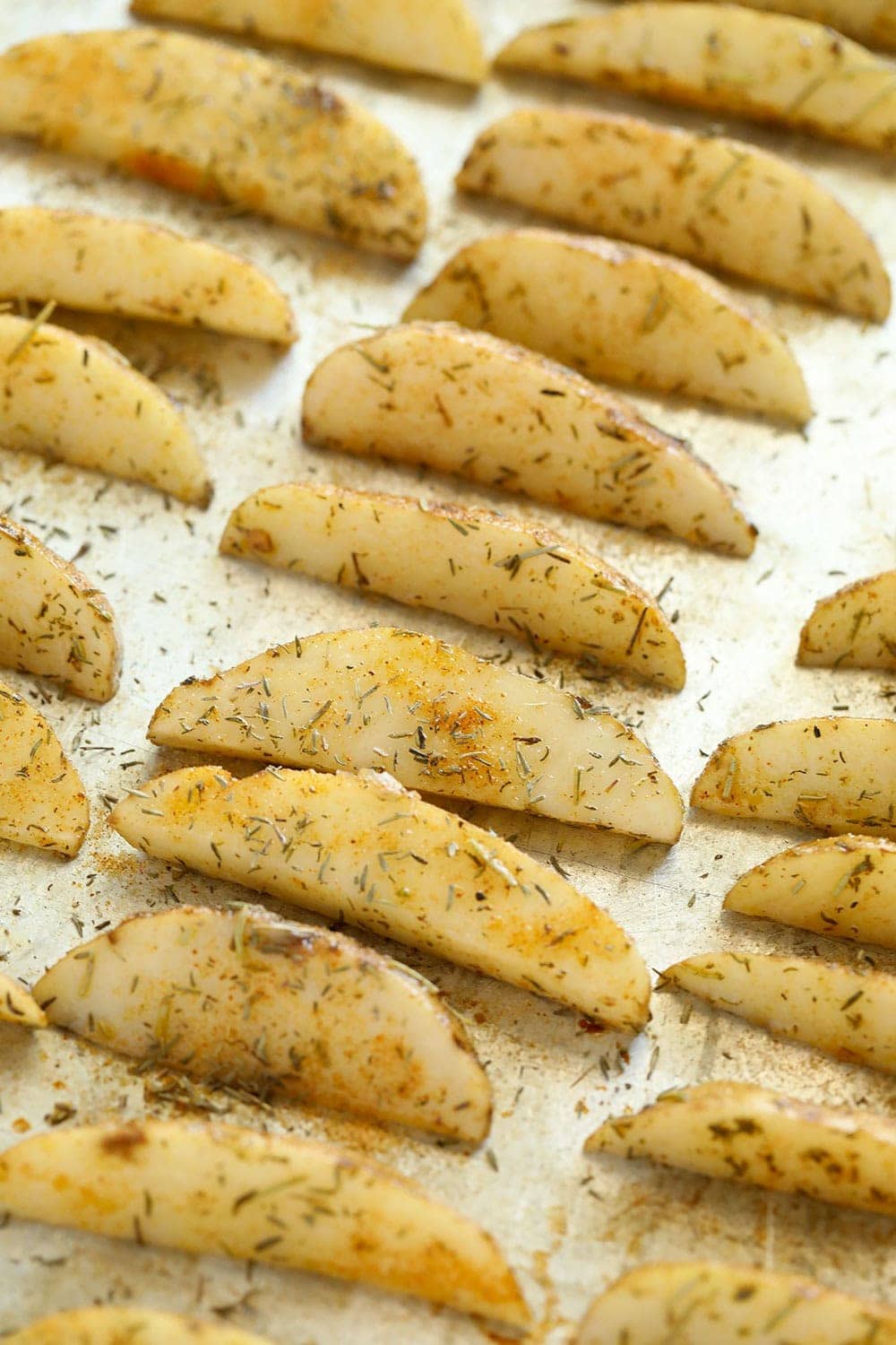 Baked potato wedges before they were baked with oil and herbs on a pan. 