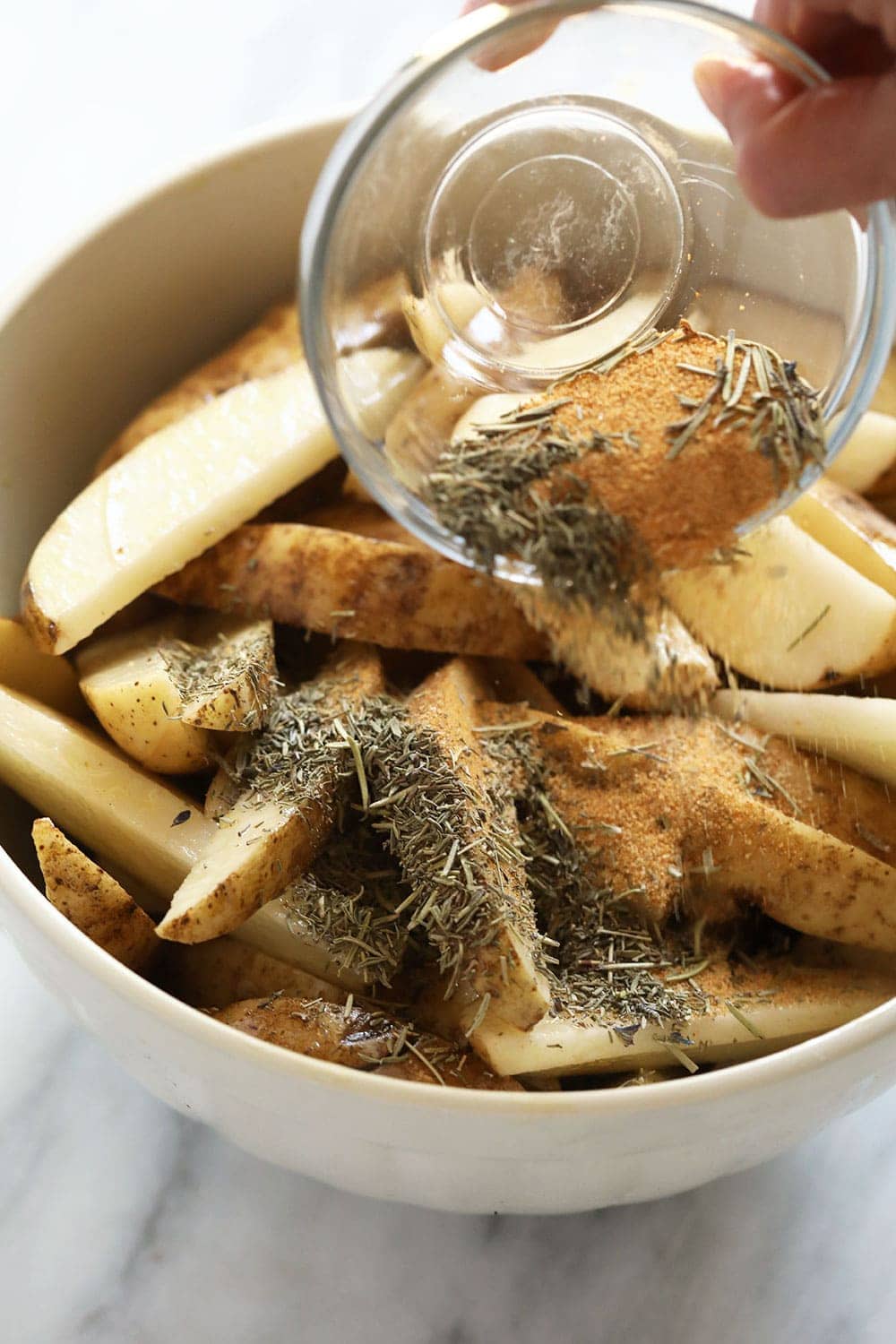 Pouring herbs and spices onto potato wedges. 