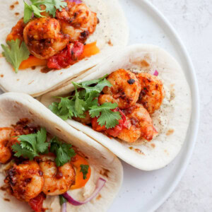 Three shrimp tacos on a white plate.