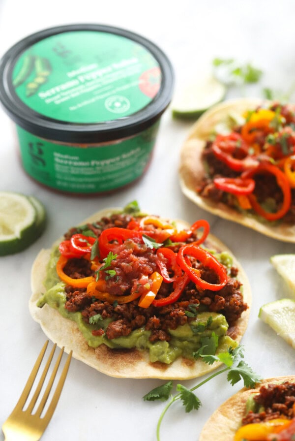 four tostada on a plate with guacamole and peppers.