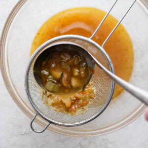 a person pouring a sauce into a strainer.