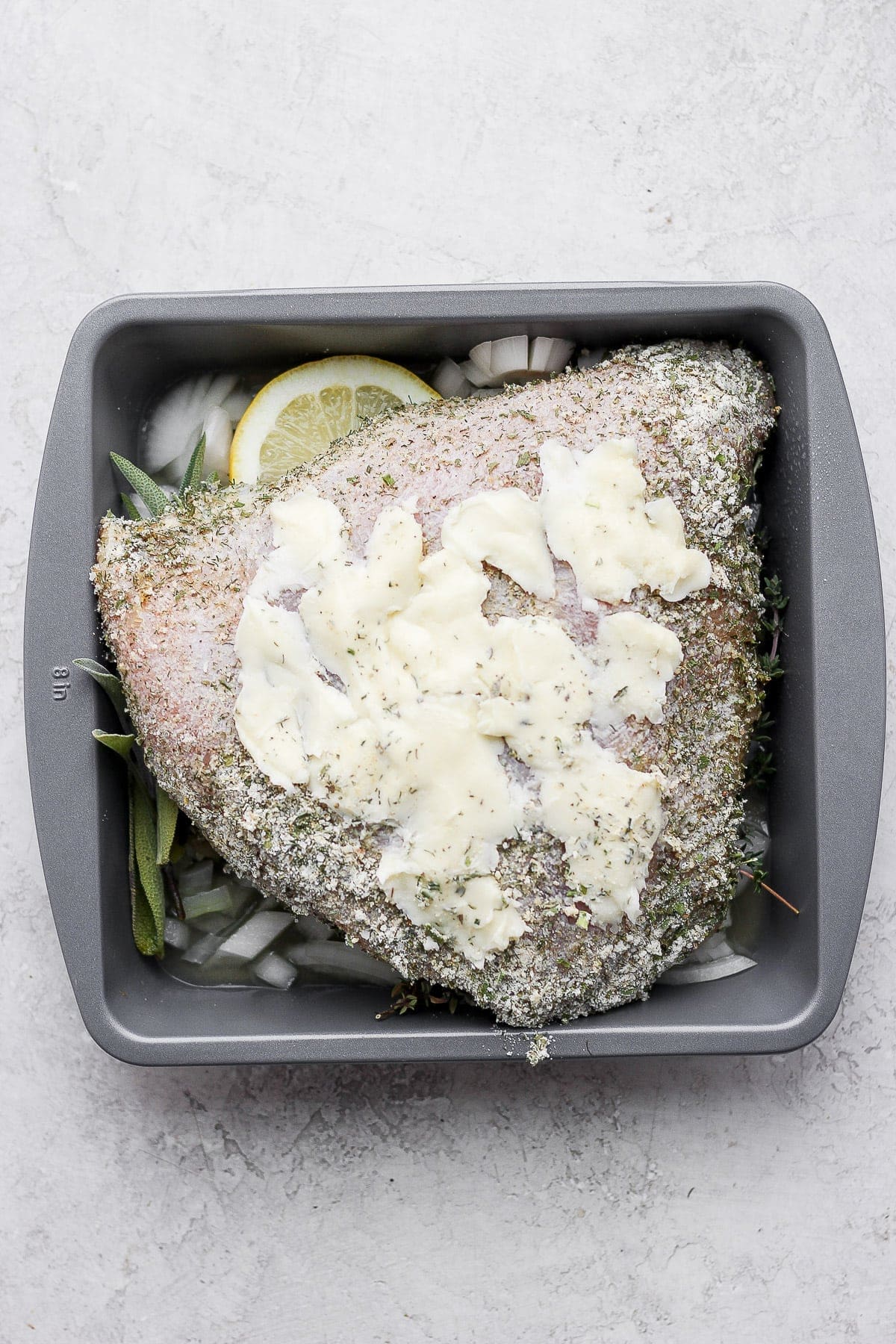 Butter, herbs, and a turkey breast in a baking dish. 