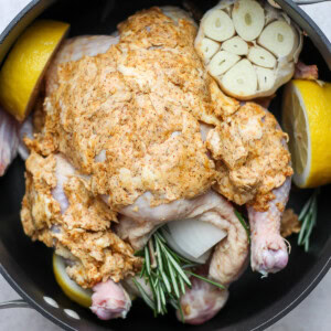 roasted whole chicken with lemons and herbs in a pan.