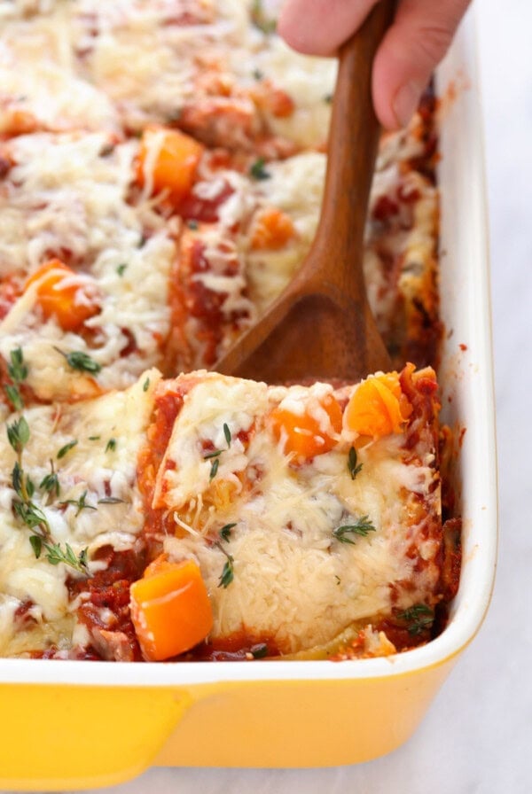 a person is scooping out lasagna from a baking dish.