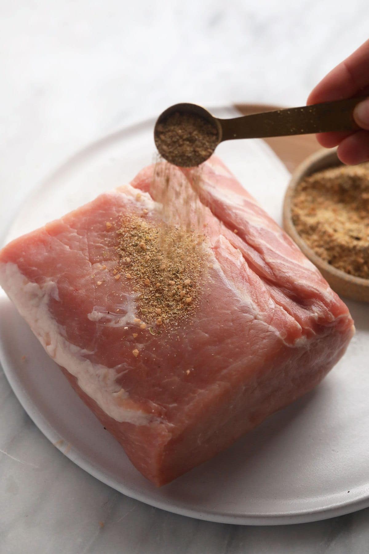 raw pork loin roast being seasoned with a pork dry rub.