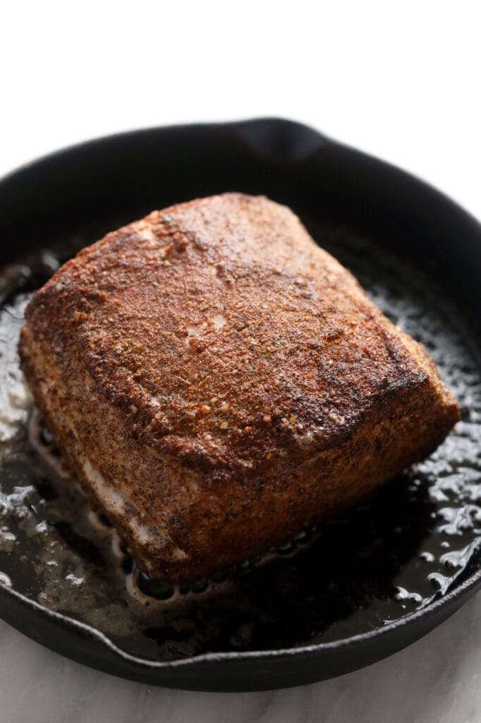 slow cooker pork loin being seared in a cast iron skillet.