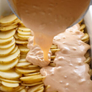 Cheesy potatoes being poured into a baking dish to make scalloped potatoes.