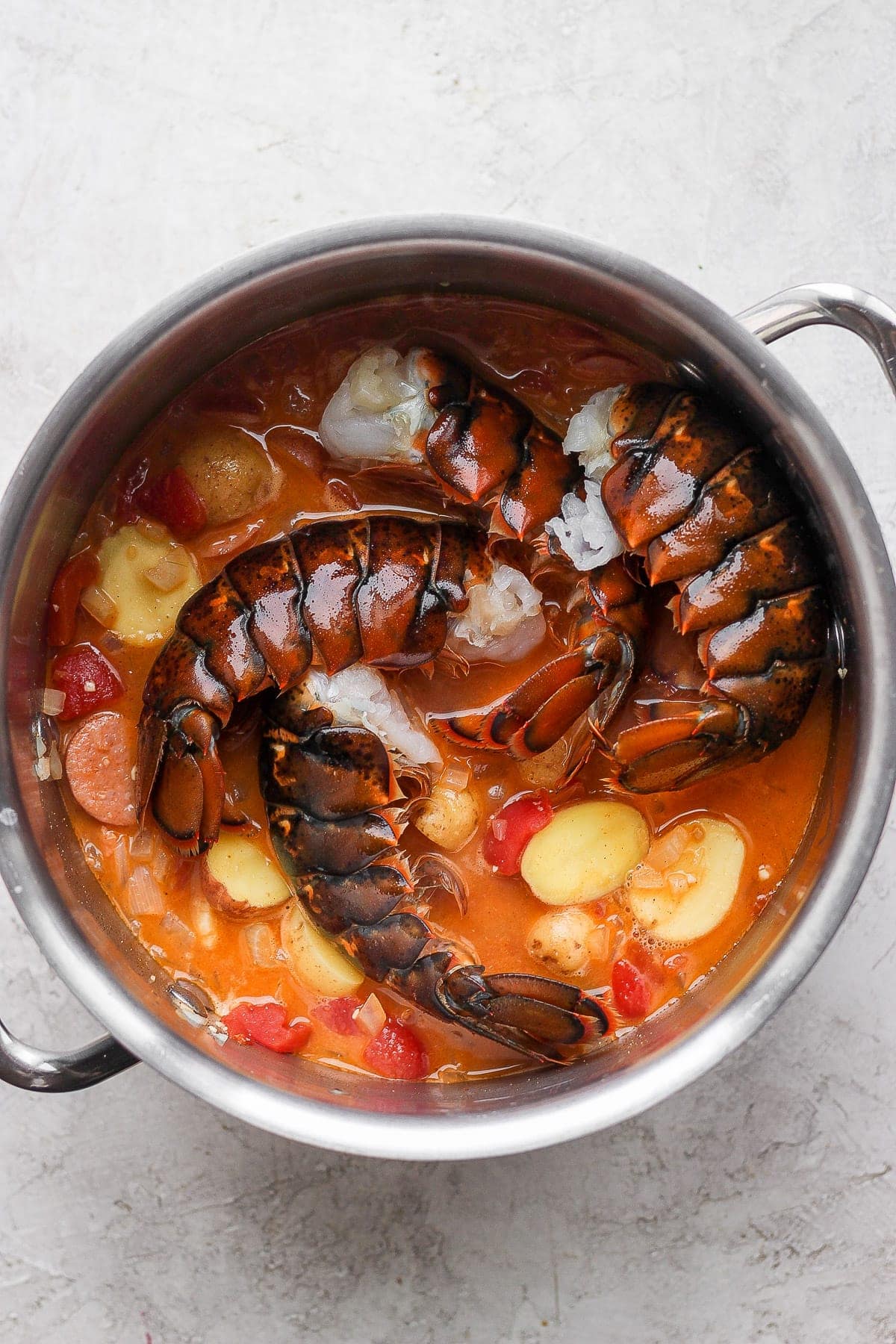 raw lobster tails being added to the seafood boil broth