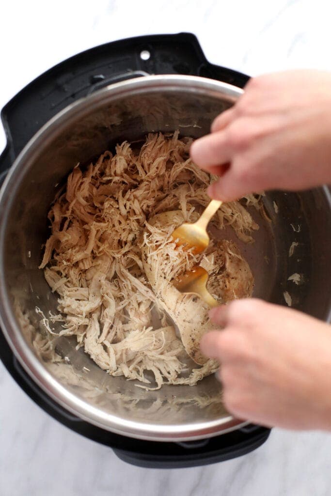 two forks shredding instant pot chicken breasts into shredded chicken.